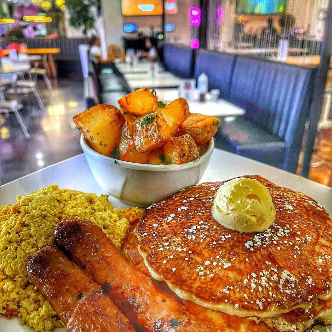 A breakfast platter with a vegan sausage, home fries, and a stack pancakes.